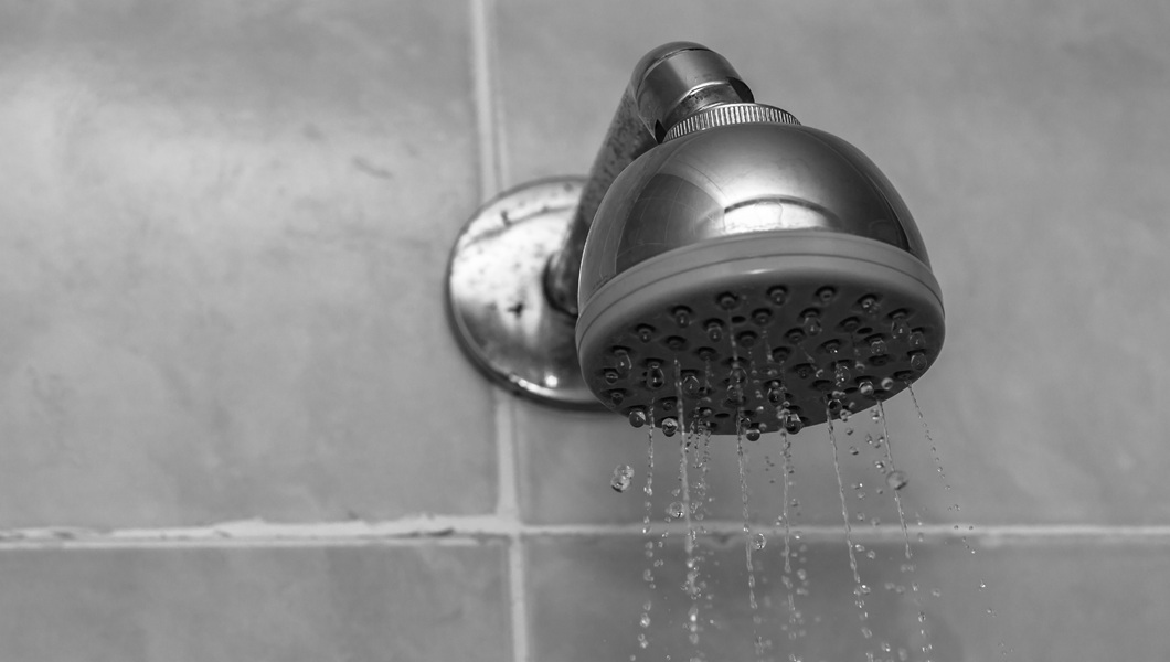 Closeup grayscale shot of a showerhead with water dripping down