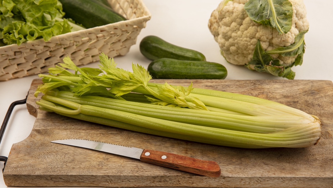 top view of celery on a wooden kitchen board with knife with cucumbers and cauliflower isolated on a white background
